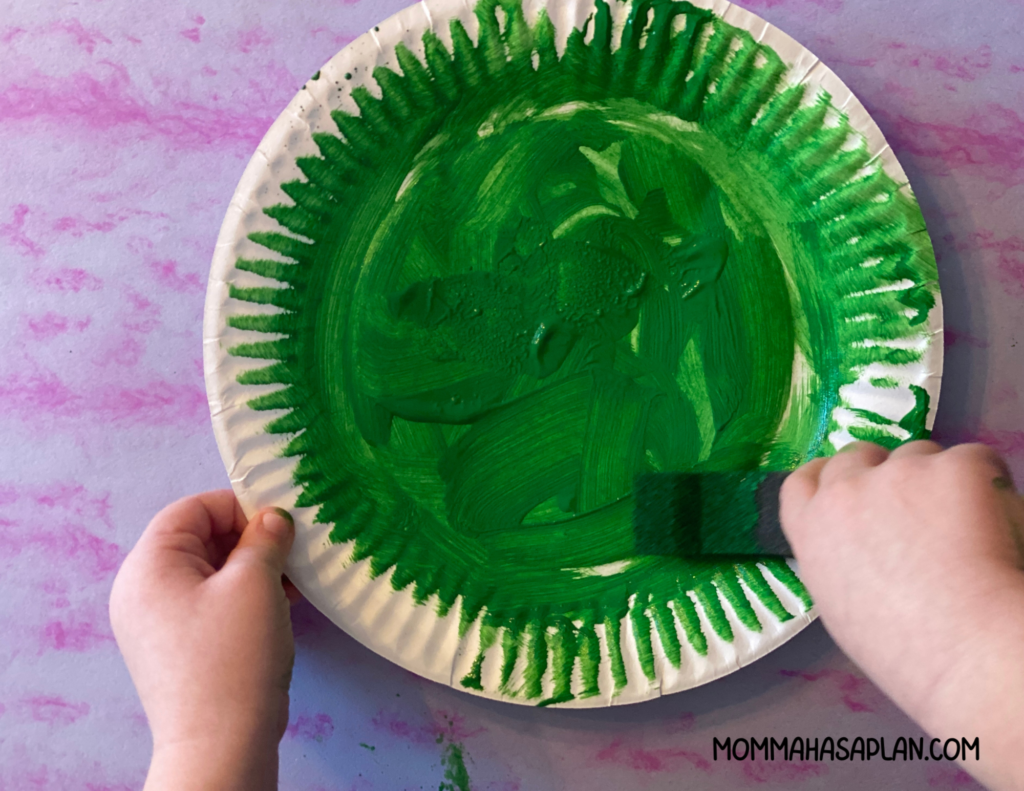 Toddler spreading green paint on plate