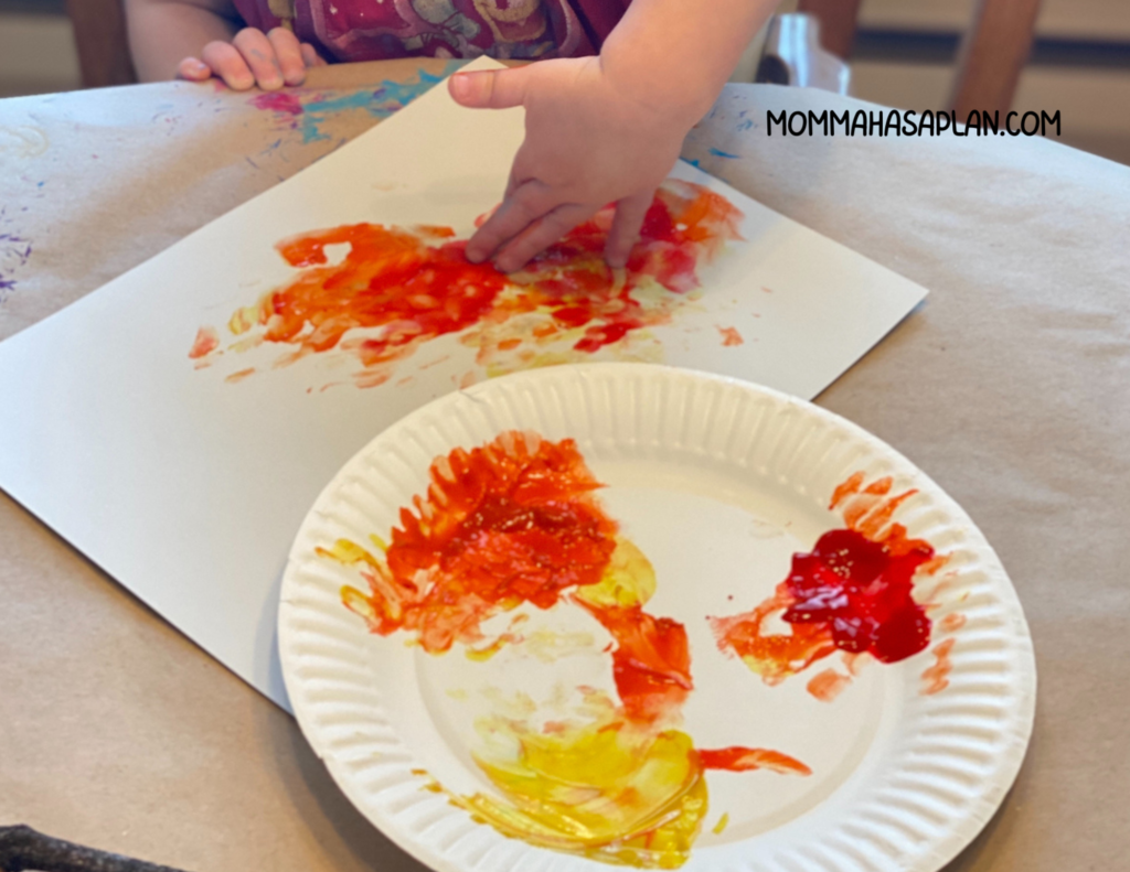 1-year-old using hand to paint a campfire with red, yellow, and orange paint