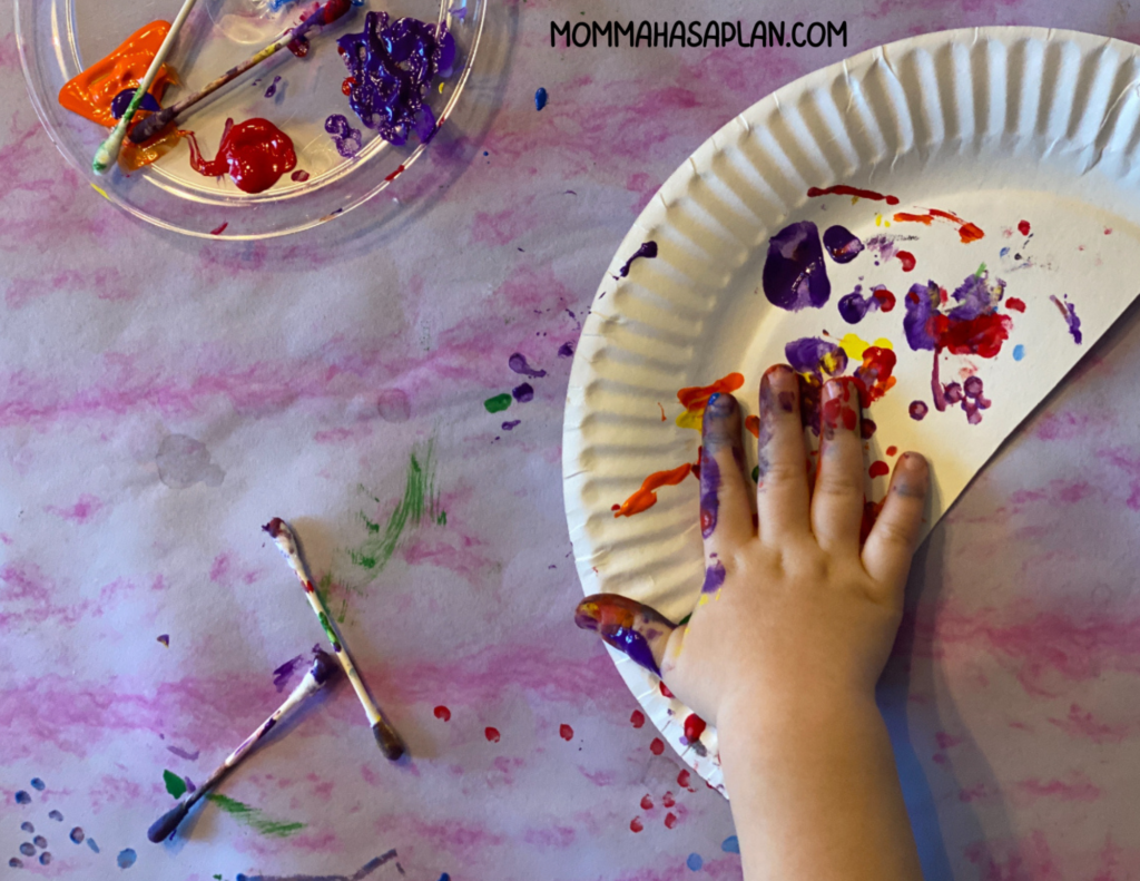 1-year-old using fingers and cotton swabs to paint a rainbow on half a paper plate 