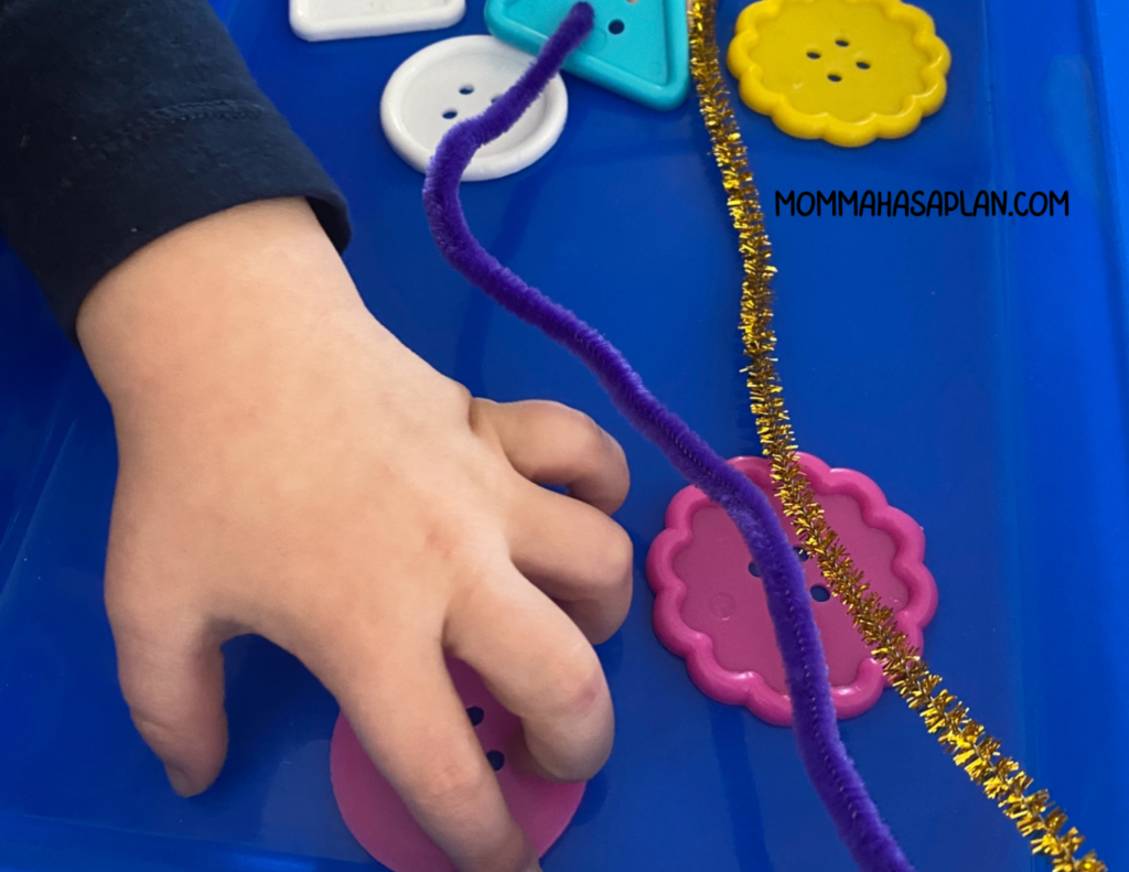 1-year-old stringing large colorful buttons on pipe cleaners