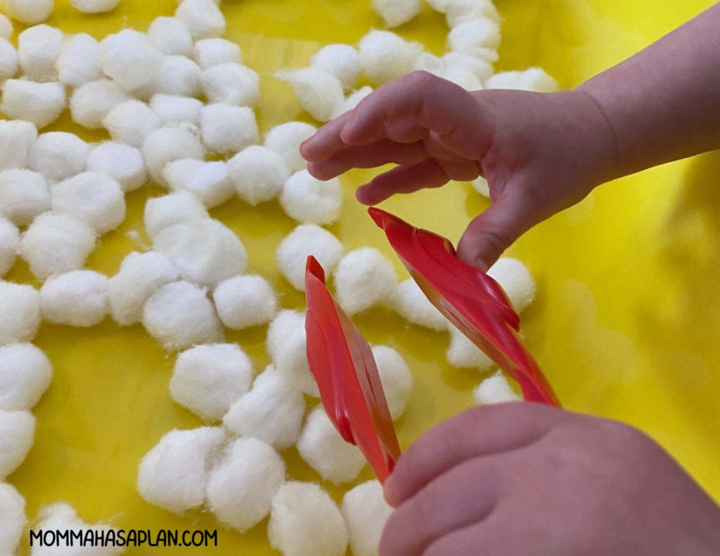 One-year-old learning to use large tweezer in cotton ball bin
