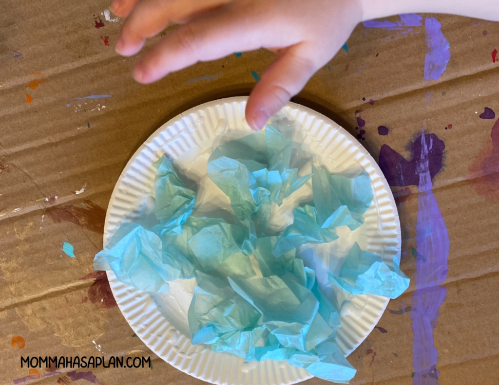 1-year-old gluing blue tissue paper to small paper plate for dr.seuss project