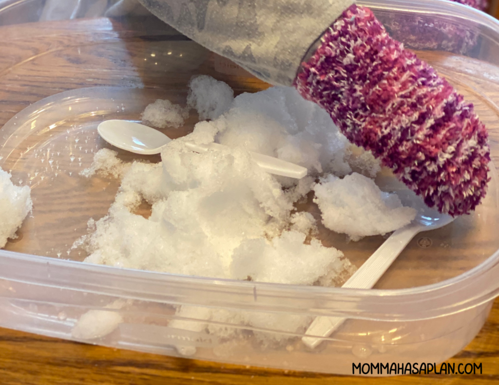 A Tupperware container with snow and spoons makes a great sensory activity for children